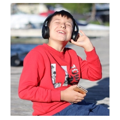 Un petit garçon amusé, avec un casque sur les oreilles connecté à son smartphone, et qui écoute un livre audio